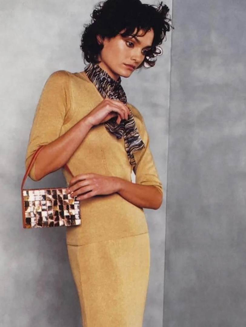 Model woman in a mustard yellow dress holding a Bottega Veneta 1997 Rare Vintage Canvas Top Handle Bag patterned mother of pearl vintage handbag against a plain background editorial magazine