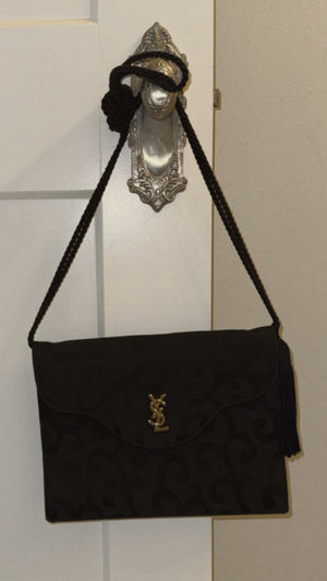 Black handbag with a gold clasp on a white door