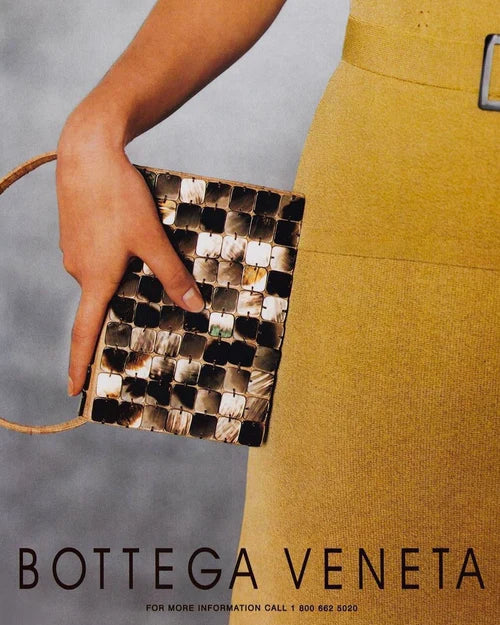 Model hand in a mustard yellow dress holding a Bottega Veneta 1997 Rare Vintage Canvas Top Handle Bag patterned mother of pearl vintage handbag against a plain background editorial magazine