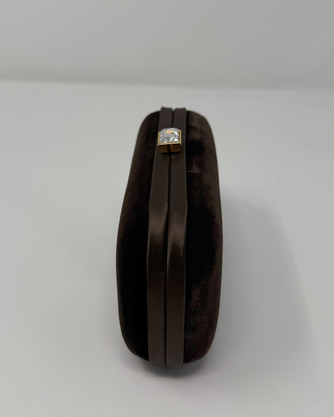 Brown velvet clutch bag with a decorative crystal clasp on a light gray background