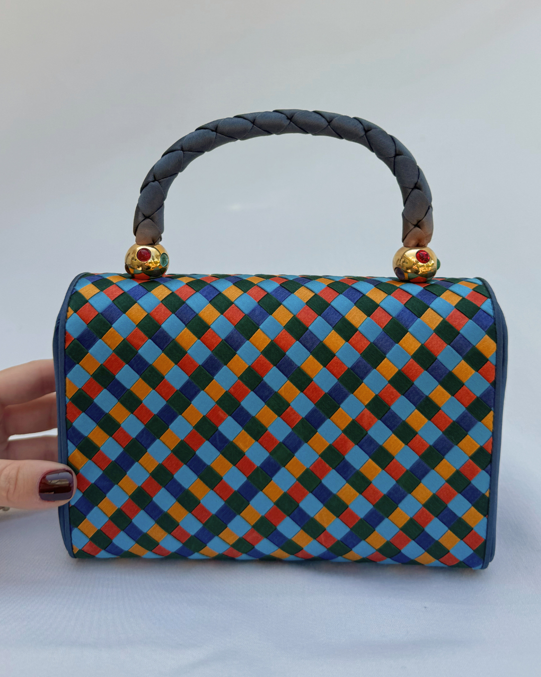 Colorful checkered handbag with braided handle held by a hand on a white background