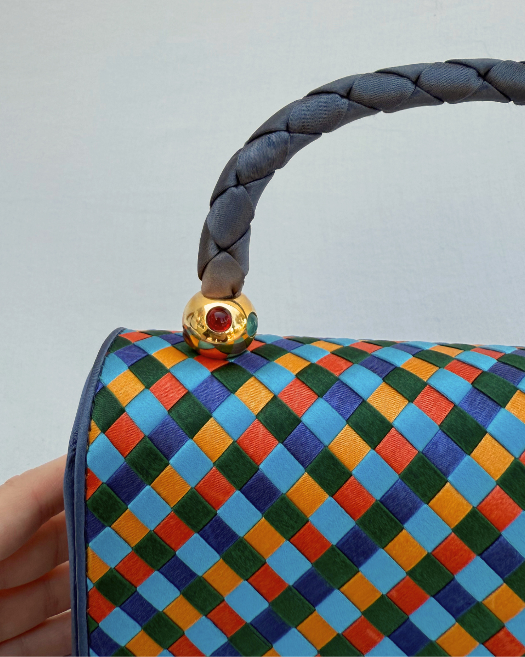 Colorful woven handbag with a braided handle against a white background