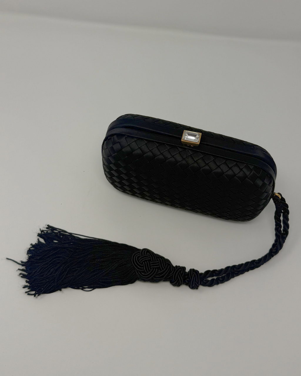 Black woven clutch with a tassel on a light gray background