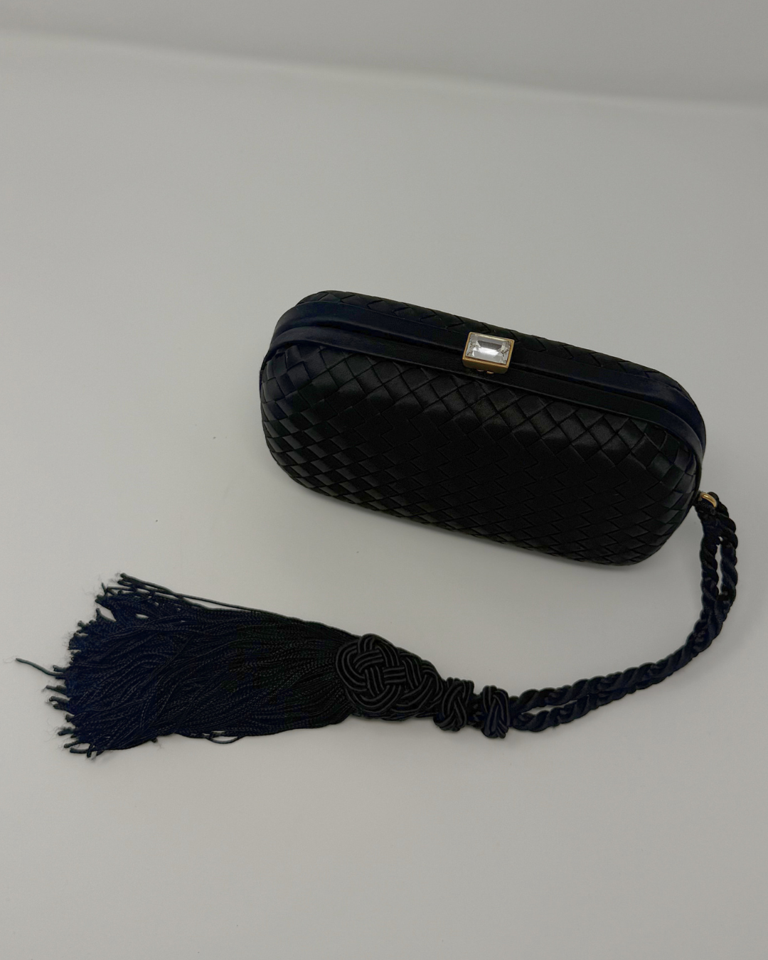 Black woven clutch with a tassel on a light gray background