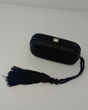 Black woven clutch with a tassel on a light gray background