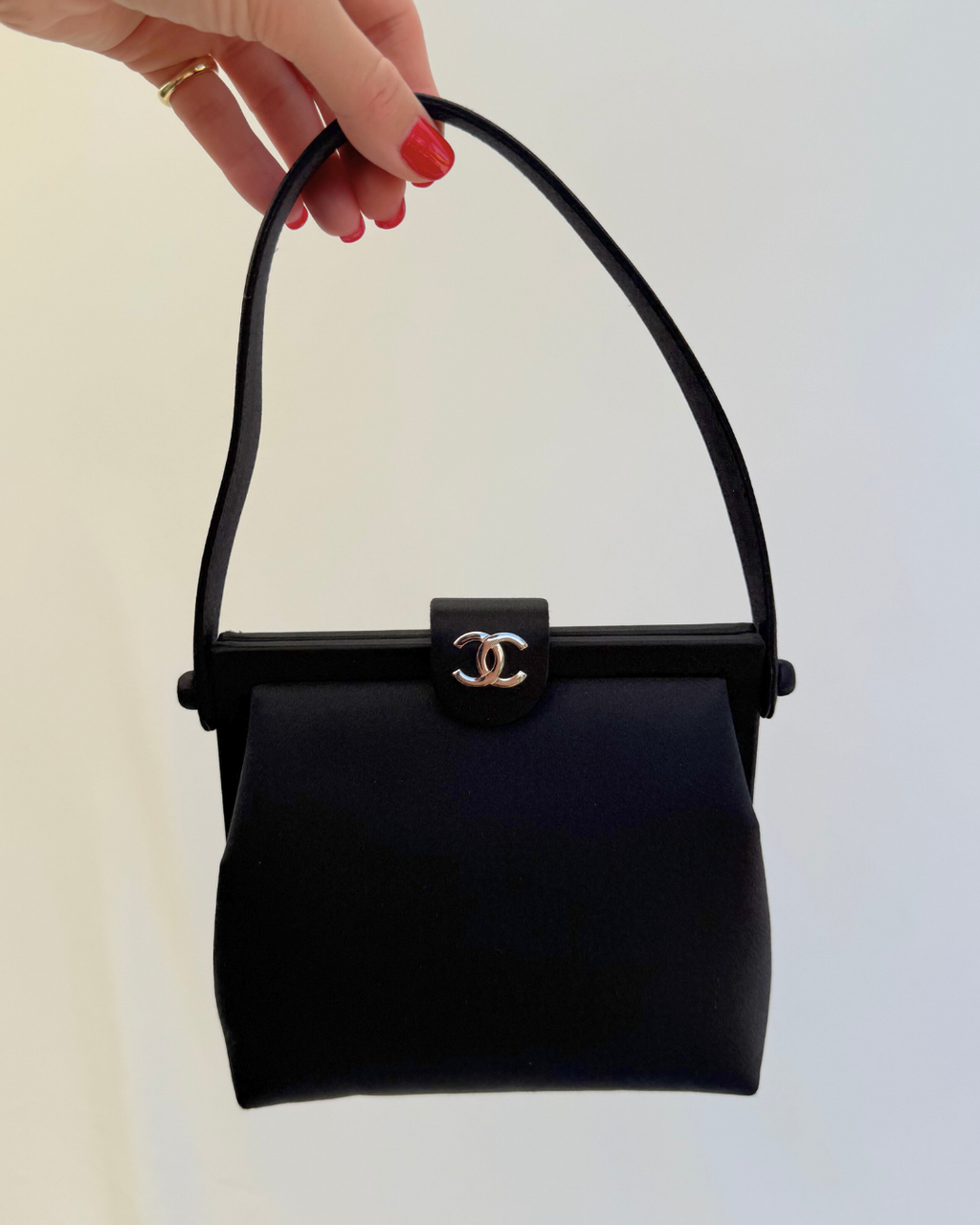Front view of Chanel Rare Vintage 1997 Mini Black Satin Frame Evening Bag with model hand on white background