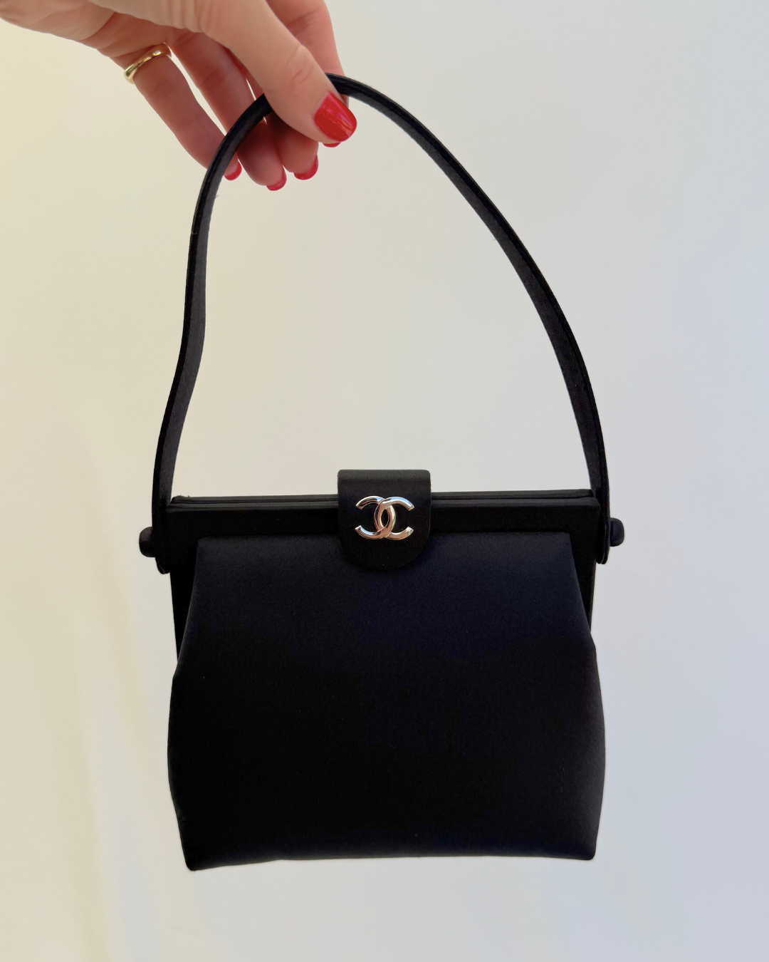 Front view of Chanel Rare Vintage 1997 Mini Black Satin Frame Evening Bag with model hand on white background