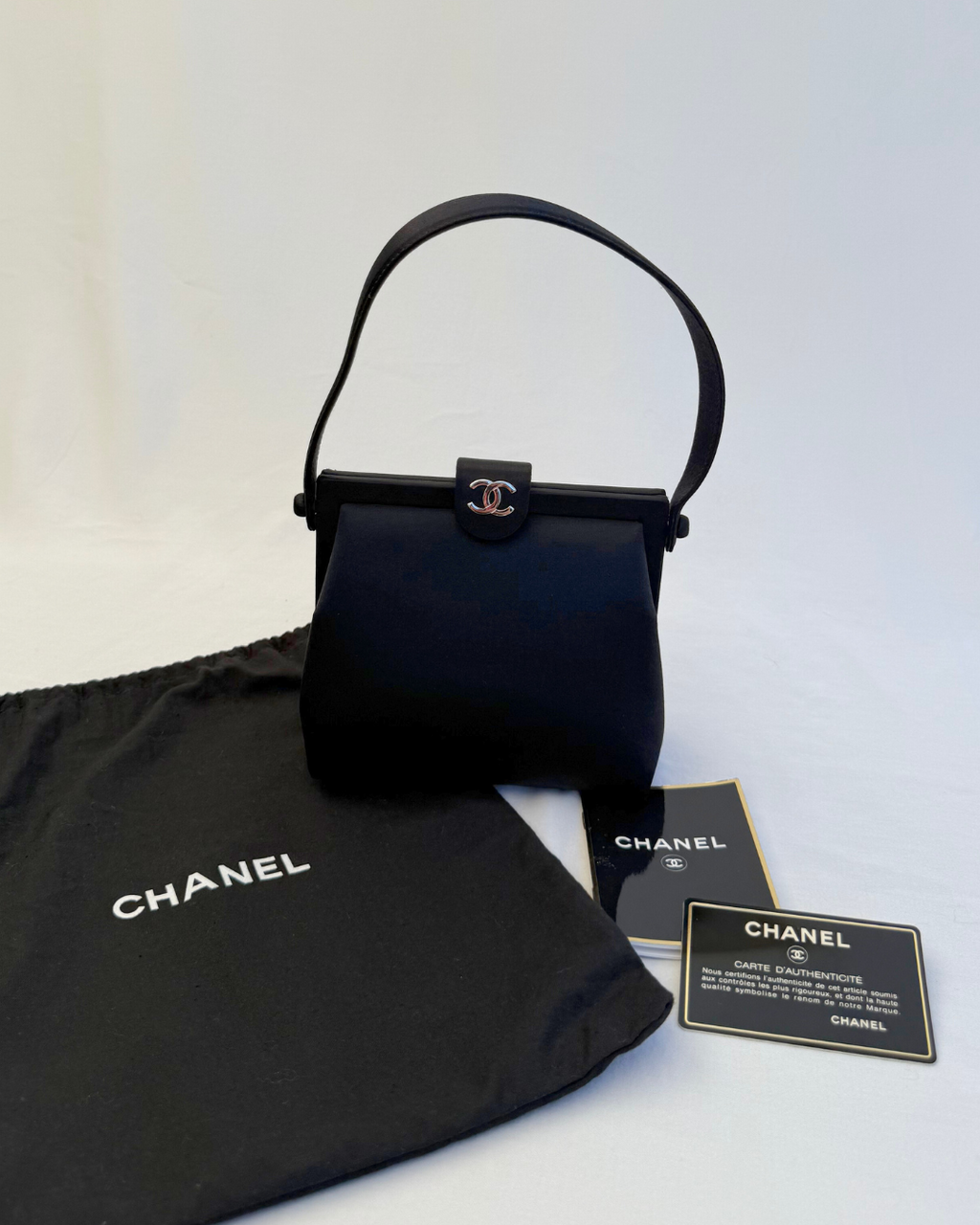 Front view with original dust cover and authenticity card for Chanel Rare Vintage 1997 Mini Black Satin Frame Evening Bag on white background