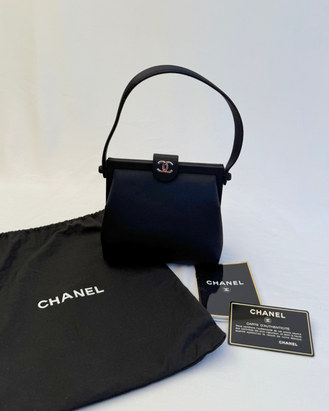 Front view with original dust cover and authenticity card for Chanel Rare Vintage 1997 Mini Black Satin Frame Evening Bag on white background