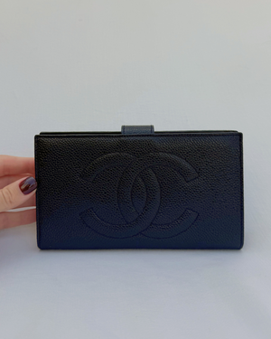 Black leather wallet with Chanel logo held by a hand on a white background
