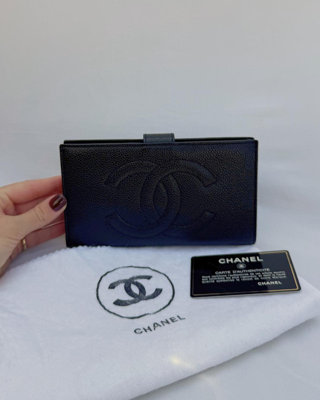 Black Chanel wallet held by a hand on a white surface with original Chanel dust cover and authenticity card