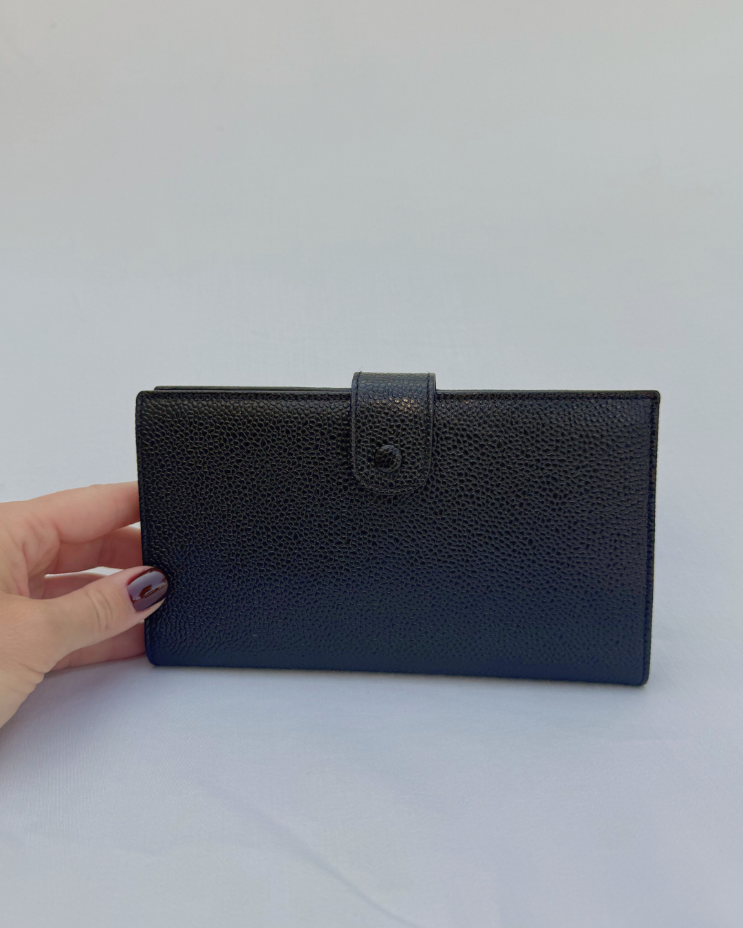 Black caviar leather vintage Chanel wallet held by a hand on a white background back view