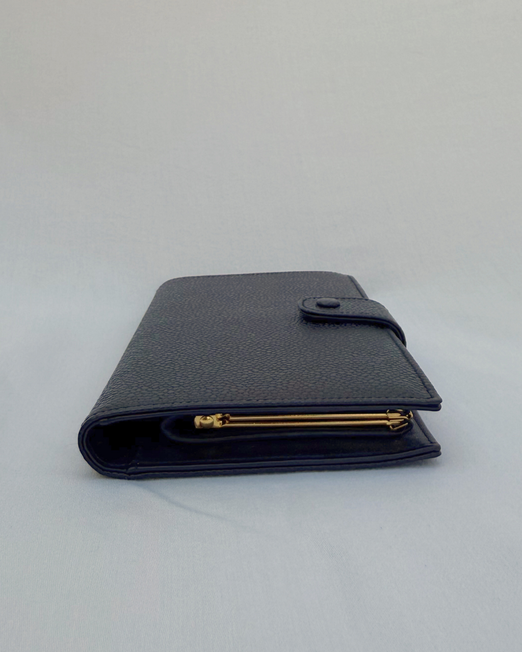 Black caviar leather vintage Chanel wallet with gold compact accents on a white background
