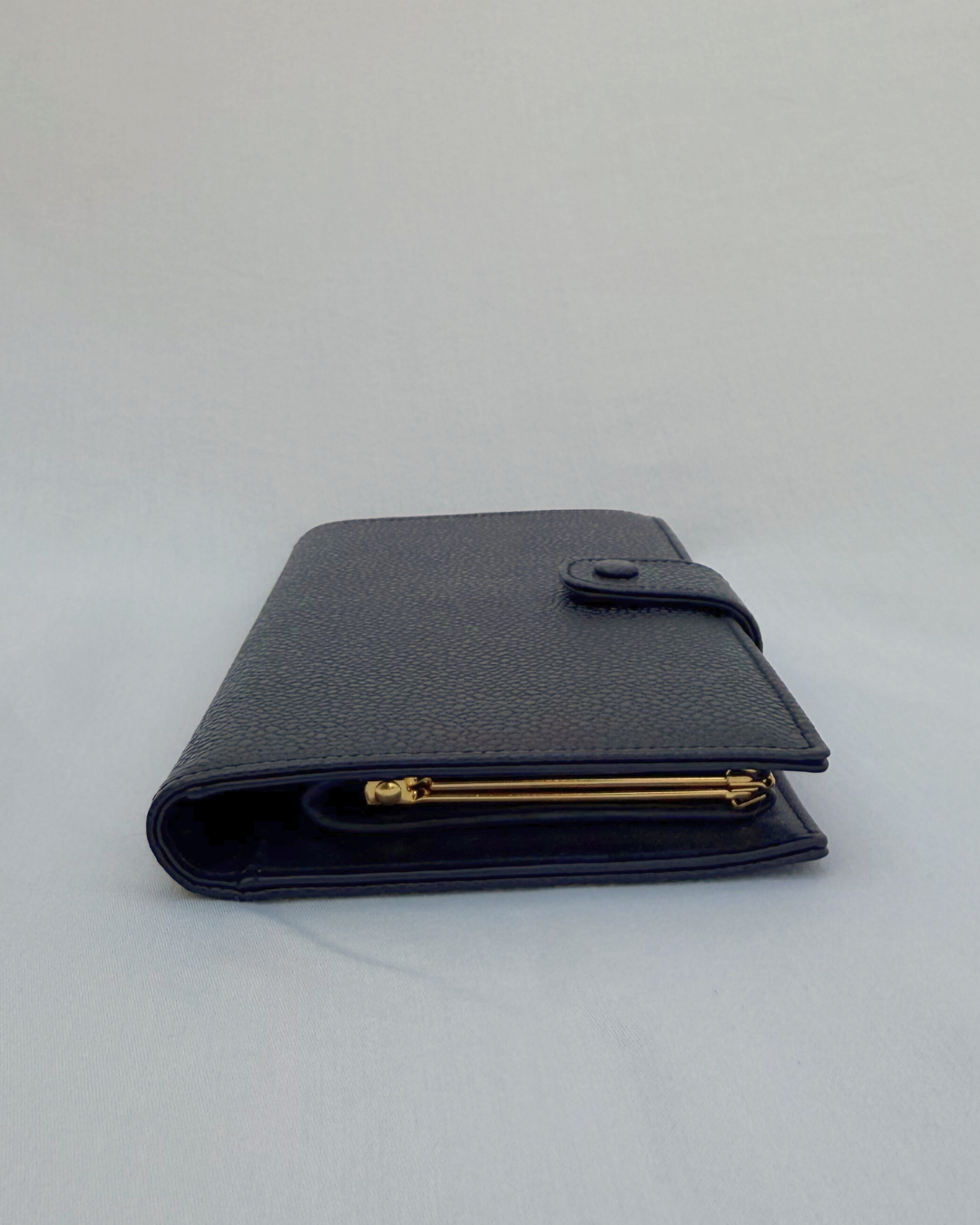 Black caviar leather vintage Chanel wallet with gold compact accents on a white background