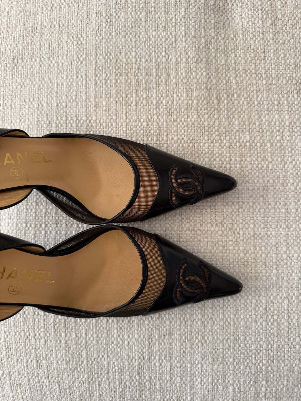 Black high-heeled shoes with Chanel logo on a textured surface