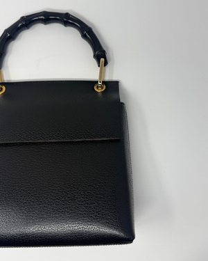 Black pebbled leather handbag with a bamboo-style top handle and gold-tone hardware, shown against a plain light background.