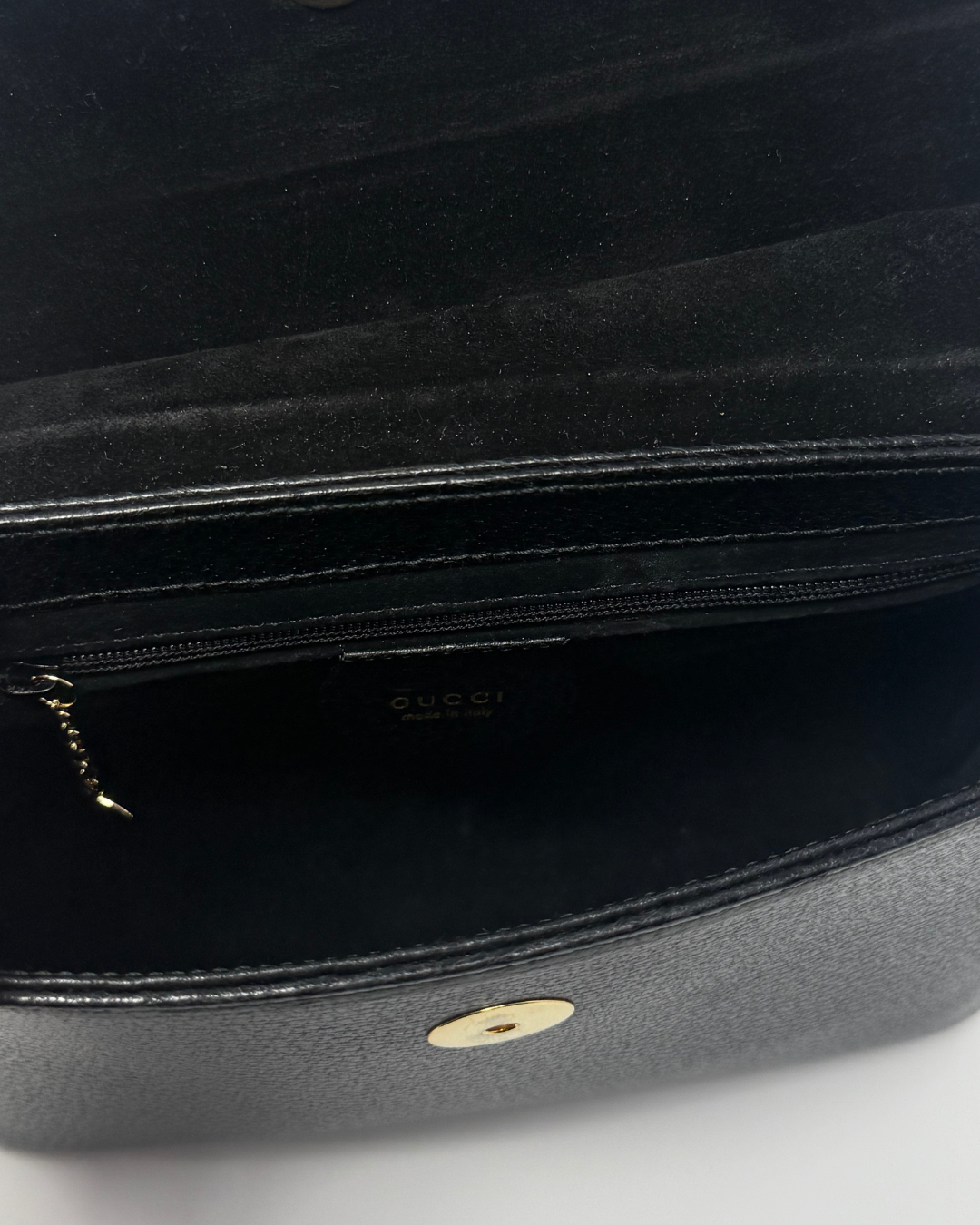 Close-up of the interior of a black Gucci handbag, showing a zippered compartment with a small gold-tone zipper pull and a gold-tone circular hardware detail on the exterior.