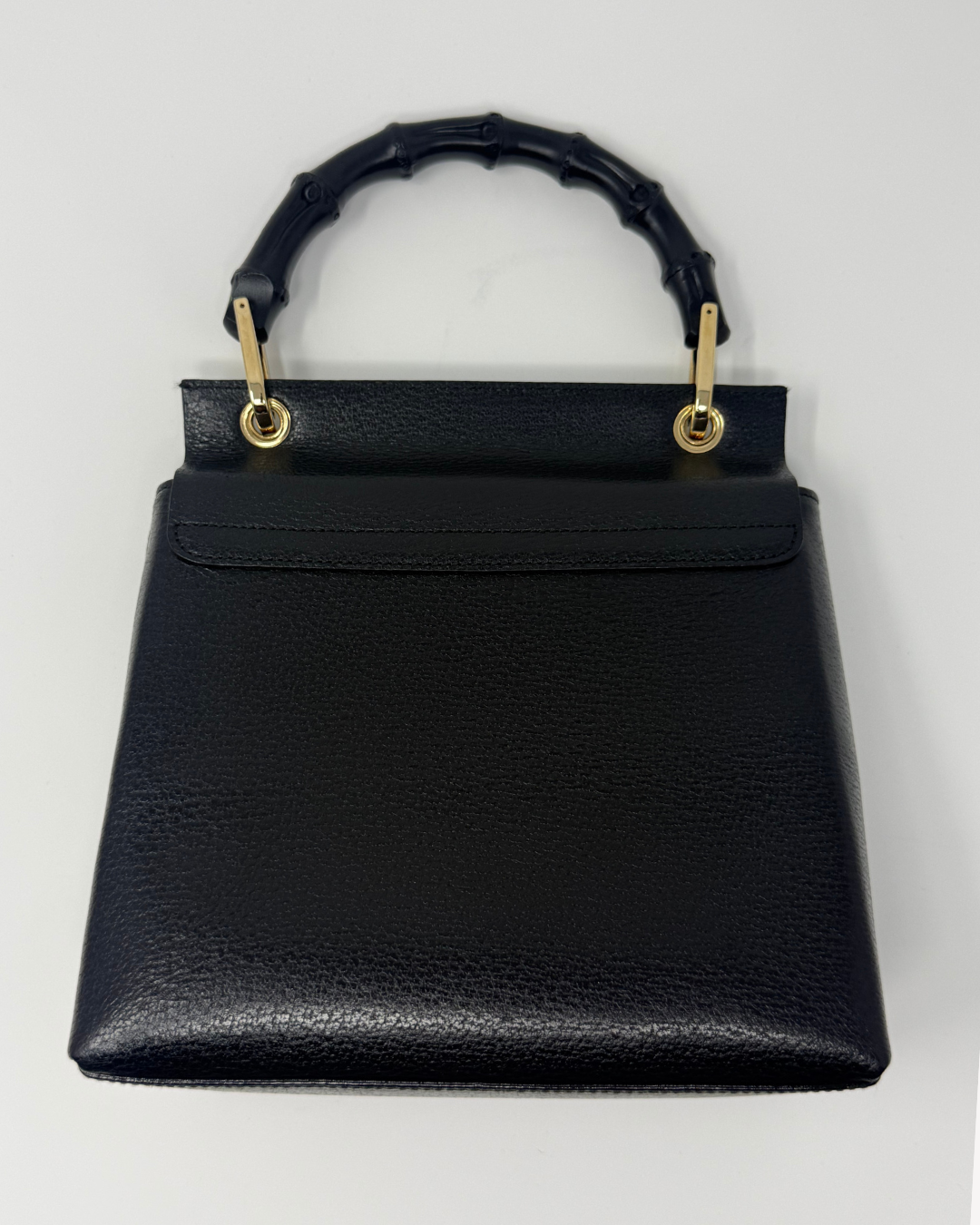 A black pebbled leather handbag with a distinctive curved bamboo-style top handle and gold-tone hardware, shown against a plain white background.