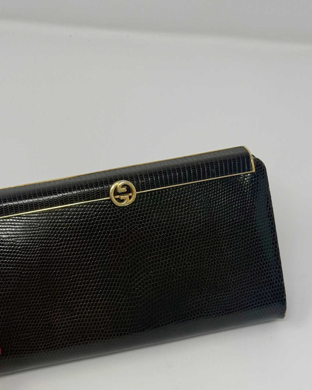 A brown textured leather clutch wallet with a gold-tone interlocking G logo clasp, shown on a plain light gray background.