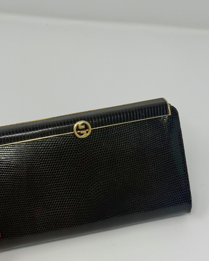 A brown textured leather clutch wallet with a gold-tone interlocking G logo clasp, shown on a plain light gray background.