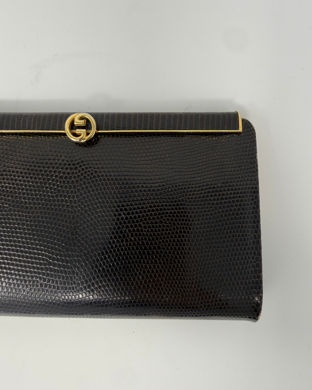 A brown textured clutch purse with a gold-tone interlocking G logo clasp, shown on a plain light background.