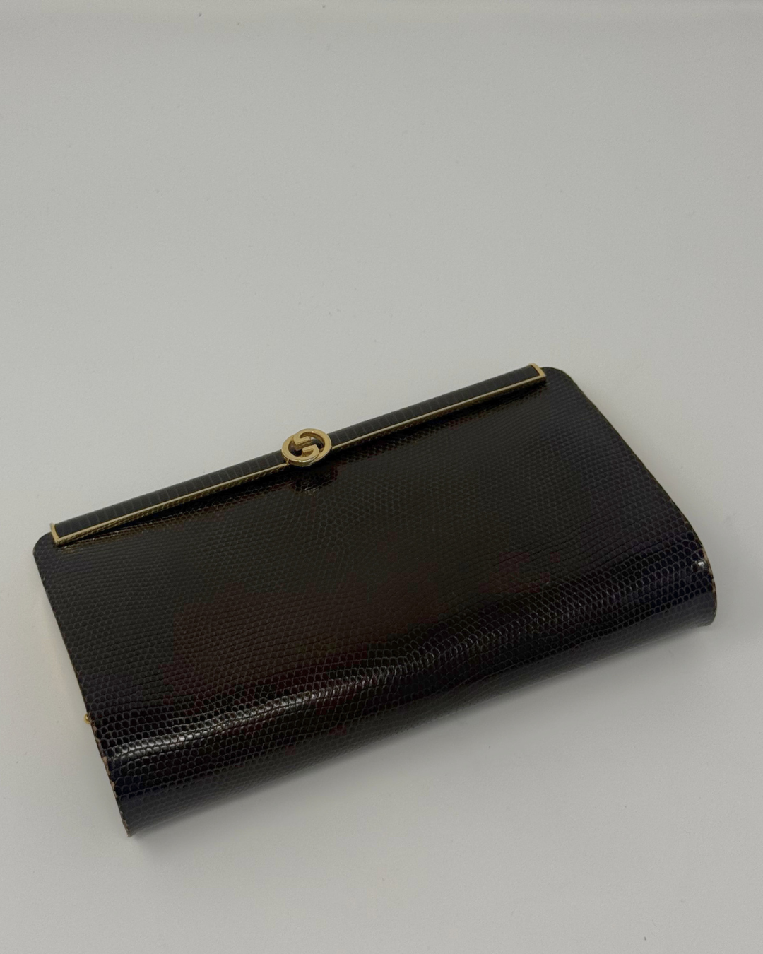 A brown textured clutch purse with a gold-tone metal frame and a circular interlocking G logo clasp, indicating the Gucci brand.