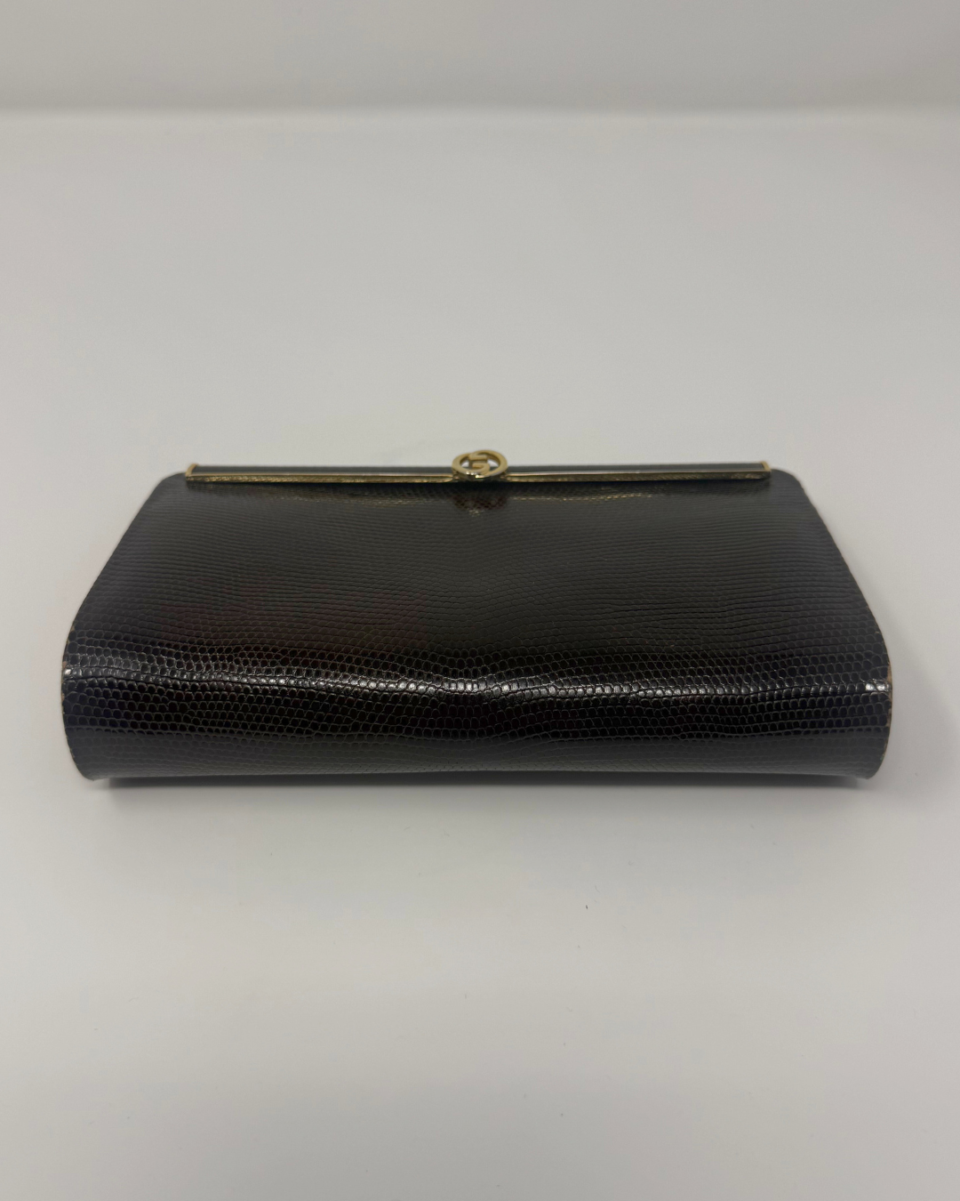 A brown textured Gucci by Tom Ford clutch purse with a gold-tone metal clasp, shown against a plain light gray background.