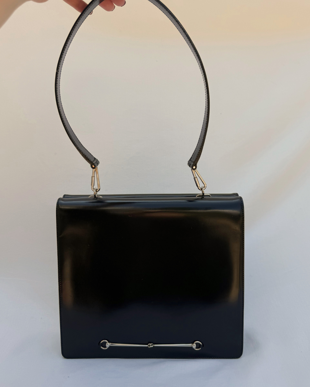 Black leather Gucci by Tom Ford vintage handbag with a handle held by a hand on a white background