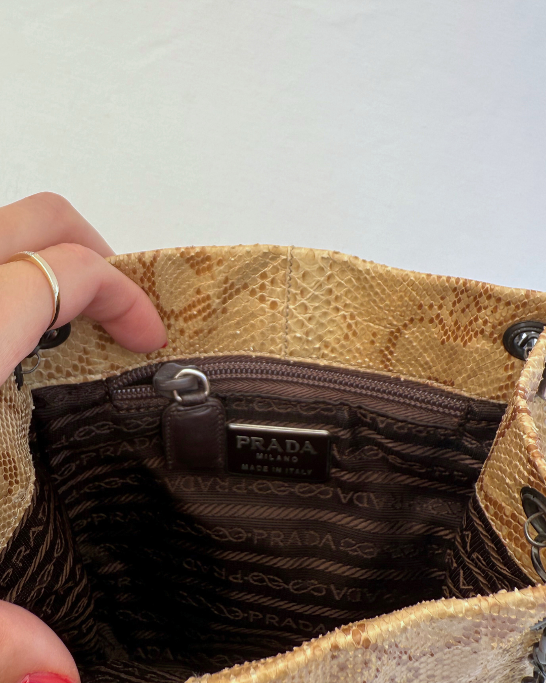 Close up of inside view of Prada Rare Vintage Enameled Metal Triangle Snakeskin Shoulder Bag satin lining on white background with model hand