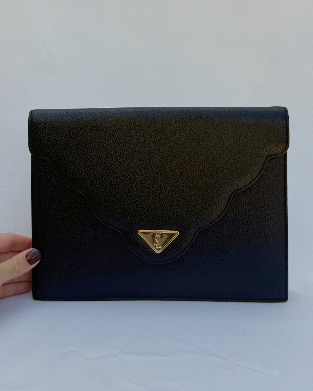 Black clutch bag with a gold triangle emblem held by a hand on a white background