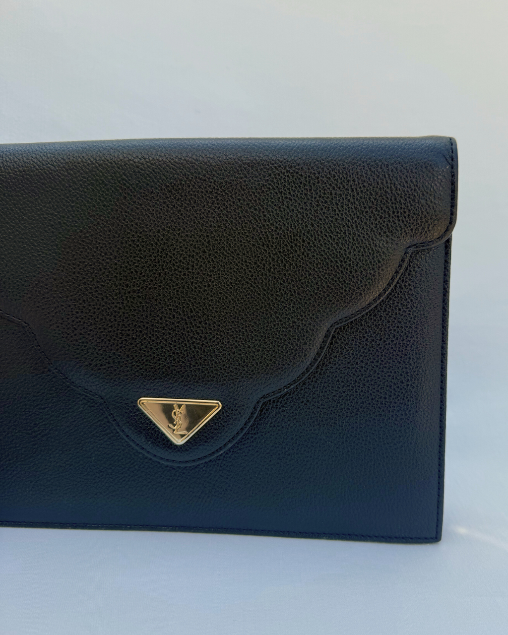Black clutch bag with a gold emblem on a white background