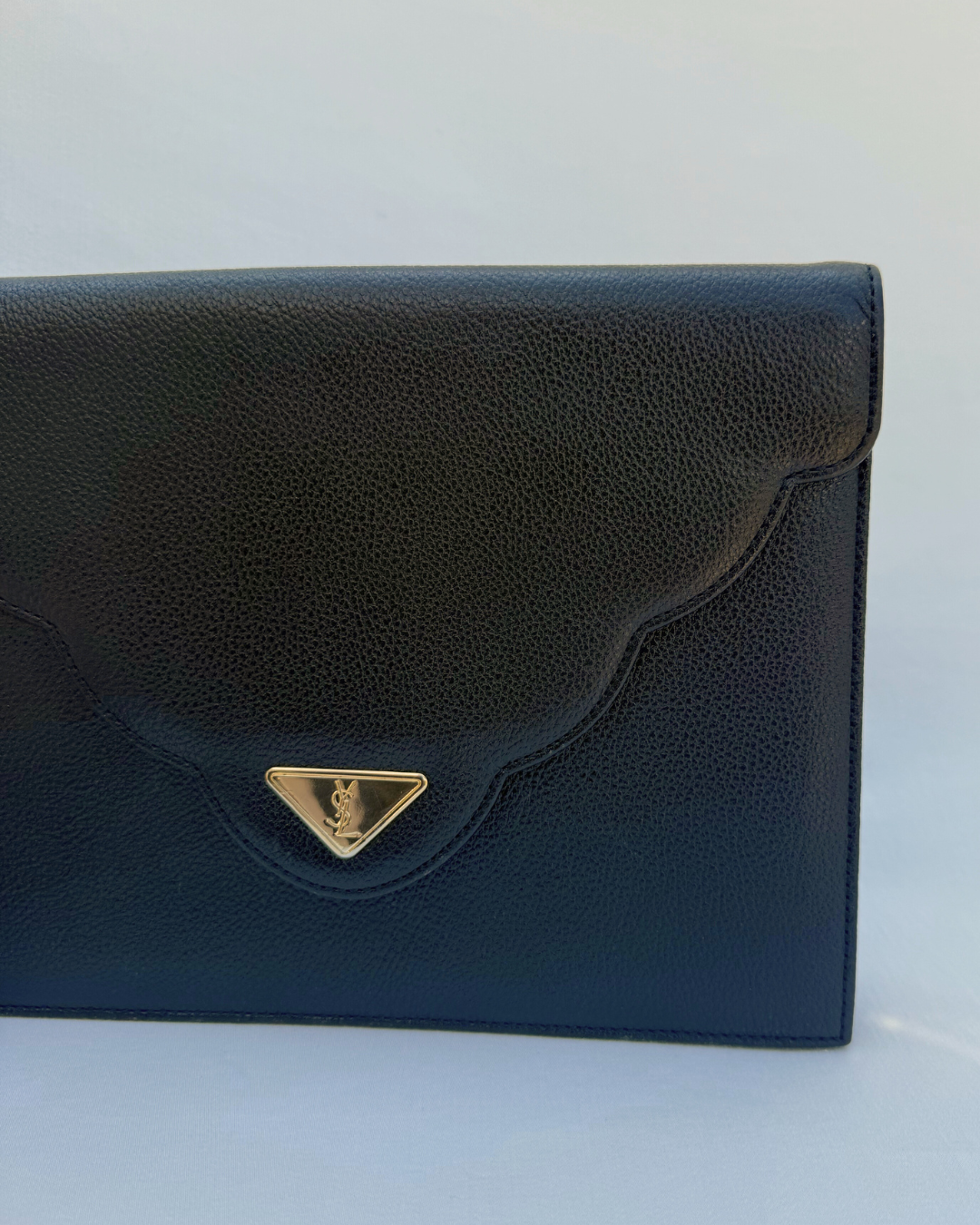 Black clutch bag with a gold emblem on a white background