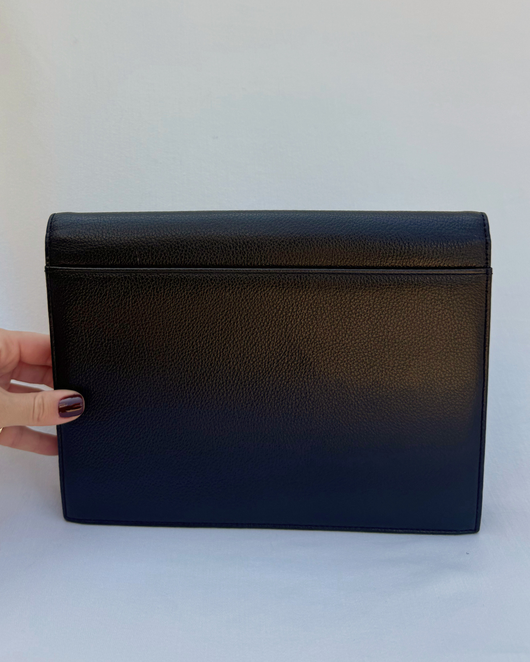 Black leather clutch held by a hand on a white background back side