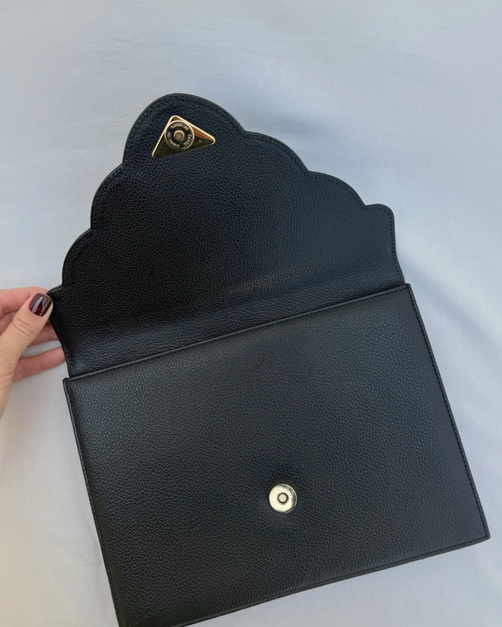 Black scalloped-edged clutch bag with gold accents on a white background