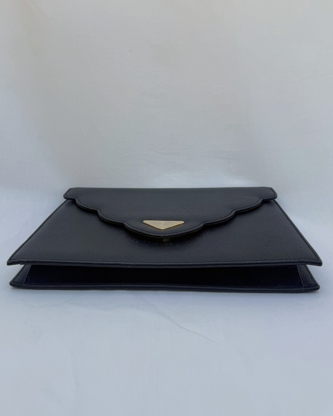 Black clutch bag with a gold emblem on a white background bottom view